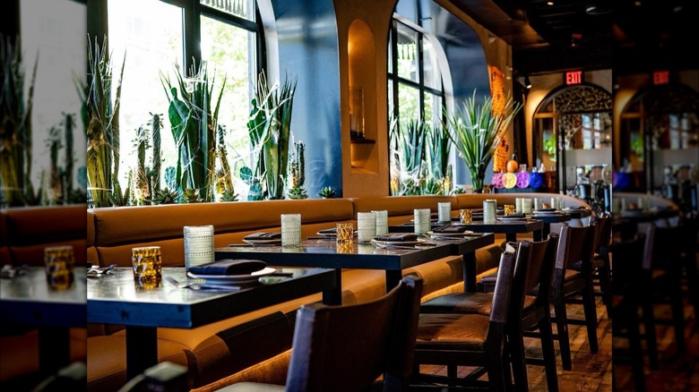 Tables set with glassware, gold booth on one side and dark chairs on other side of tables, greenery behind