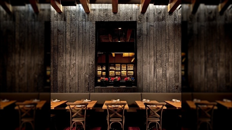 Interior of Girl & the Goat, long booth, tables, and chairs on dark wood wall with mirror