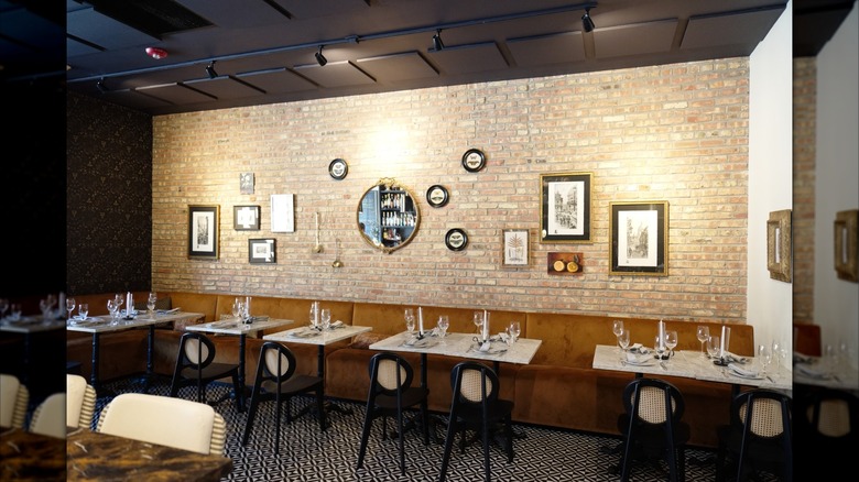 Interior of restaurant, beige brick wall with photos and mirror, white tables on beige booth