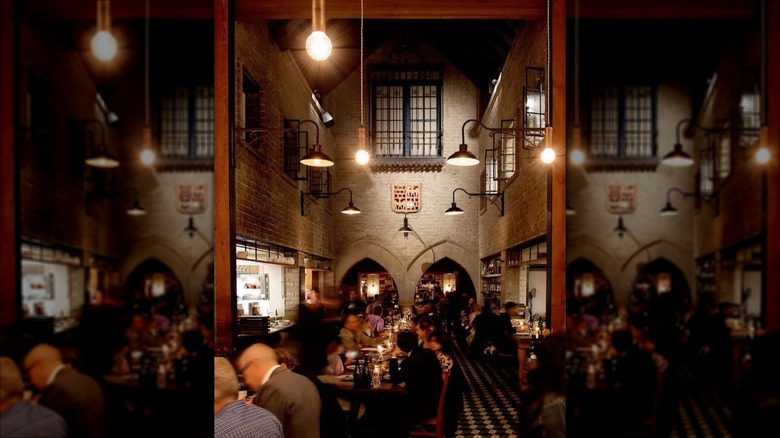 Long shot of dim restaurant, stone back wall, guests at tables blurred