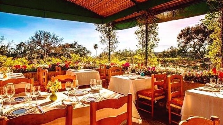 Gorgeous outdoor champagne brunch setup with white tablecloths, wine glasses, surrounded by greenery