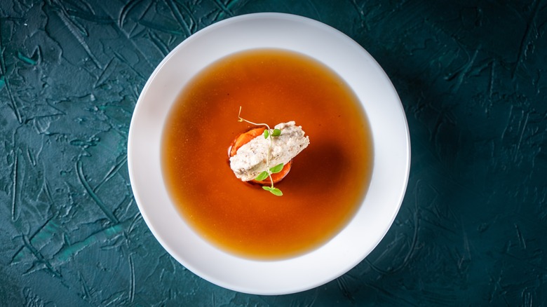 Top view of a plate of consommé with garnish against a dark background