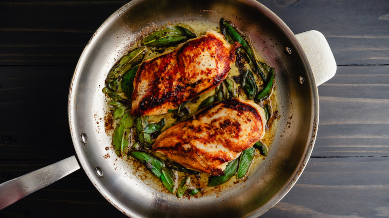 Top view of a pan with seared chicken and sage