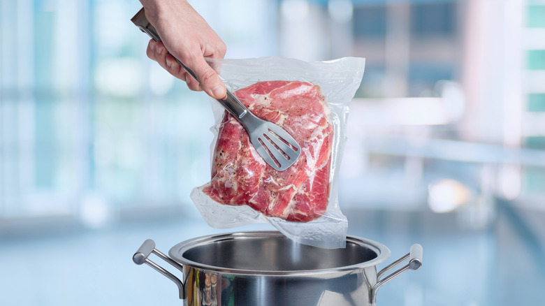 Lowering vacuum-sealed meat into a cooking pot