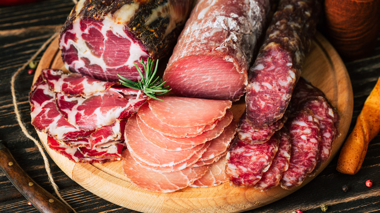 Wooden cutting board filled with whole and sliced cured meat products