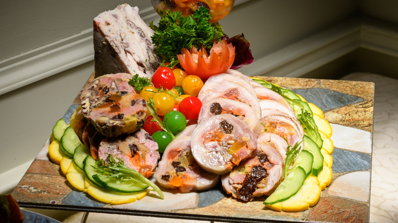 Slices of galantine arranged on slate tray along with veggies, greens, and herbs