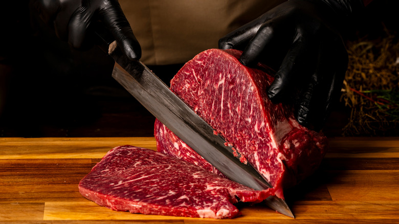 Chef wearing black gloves and slicing red meat on a wooden board