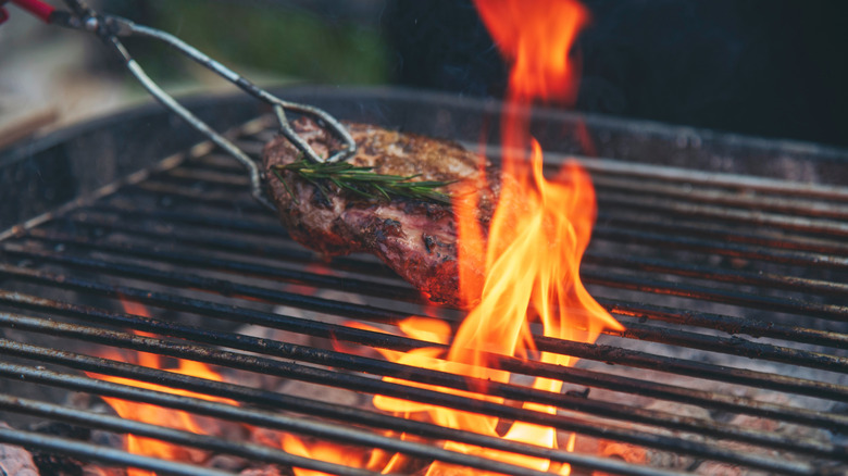 Grilling steak garnished with rosemary over an open fire grill