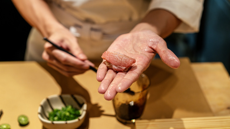 A sushi chef holding freshly prepared sushi roll
