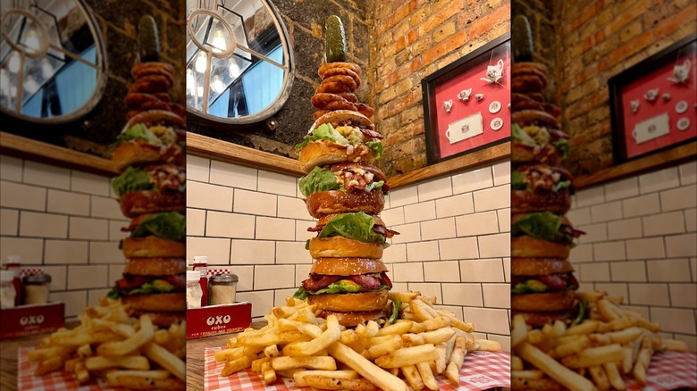 Giant stack of burgers with pile of fries on table in cafe