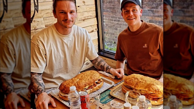 Two people sitting at a table with two giant sandwiches
