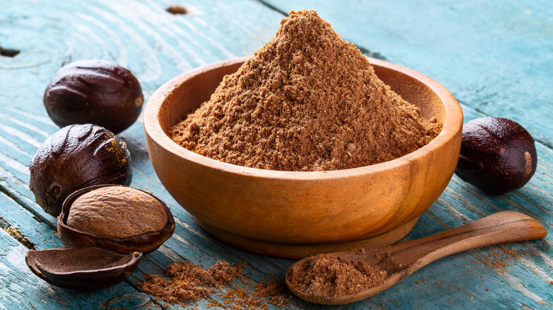 nutmeg powder in a wooden bowl with wooden spoon surrounded by nuts