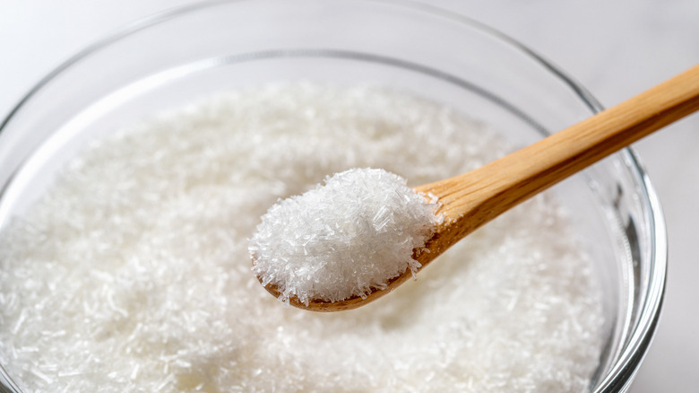 Monosodium glutamate in a wooden spoon over glass bowl