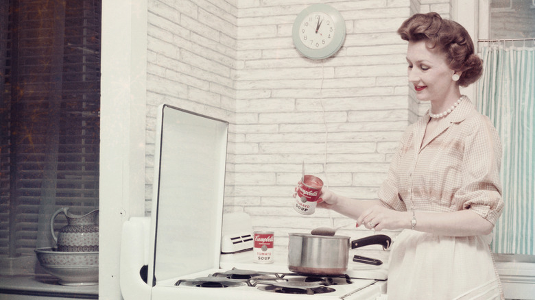 A woman cooking with cans of Campbell's tomato soup, circa 1955