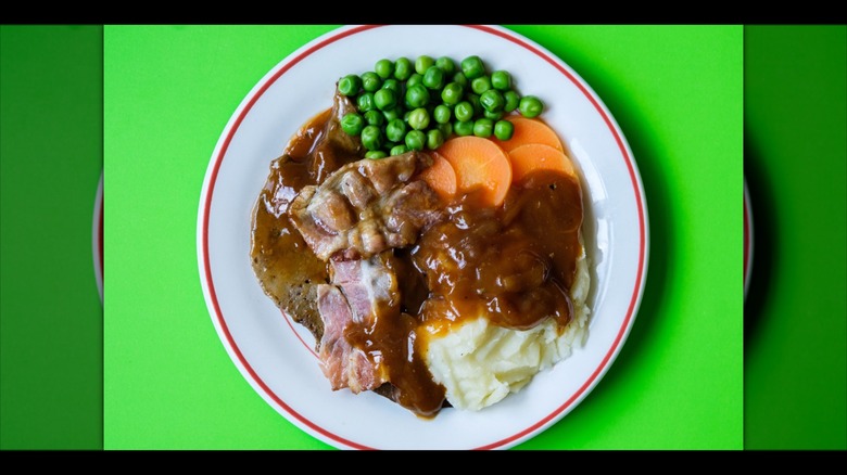 Mirrored image of liver and bacon with gravy and vegetables against green background
