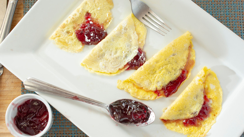 Four jelly omelettes on a white plate with more jelly on the side