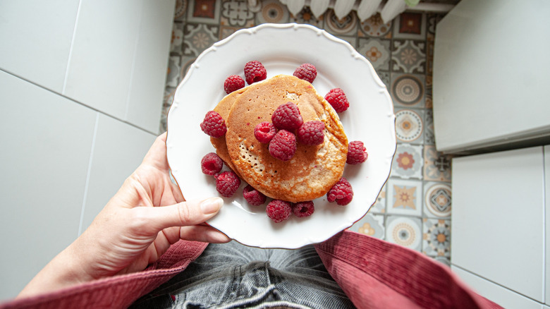 A person holds plate of whole wheat pancakes in a home kitchen