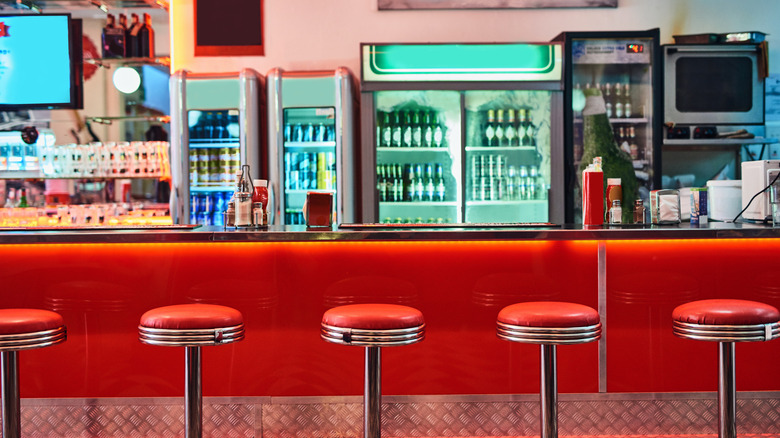 Red bar stools at a colorful retro diner counter with coolers in background