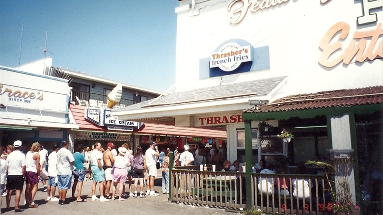 Exterior of Thrasher's with a line of people on a sunny day