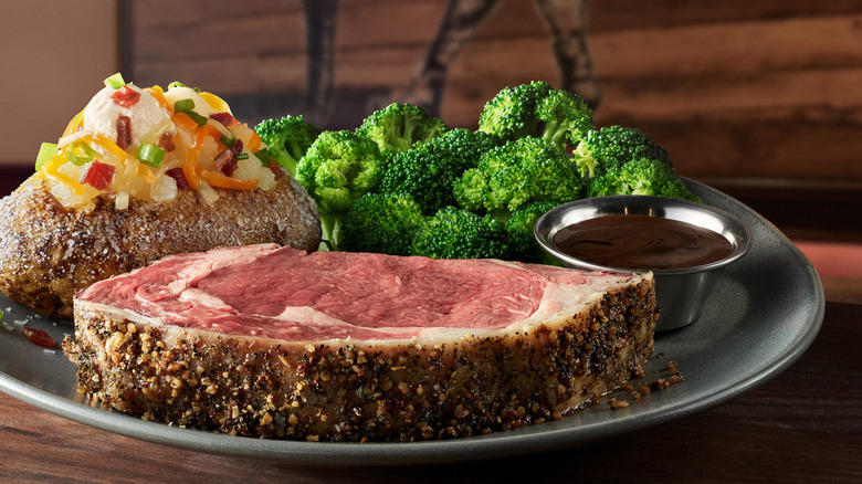 Classic Prime Rib from Outback Steakhouse with broccoli, loaded baked potato, and cup of sauce on silver plate