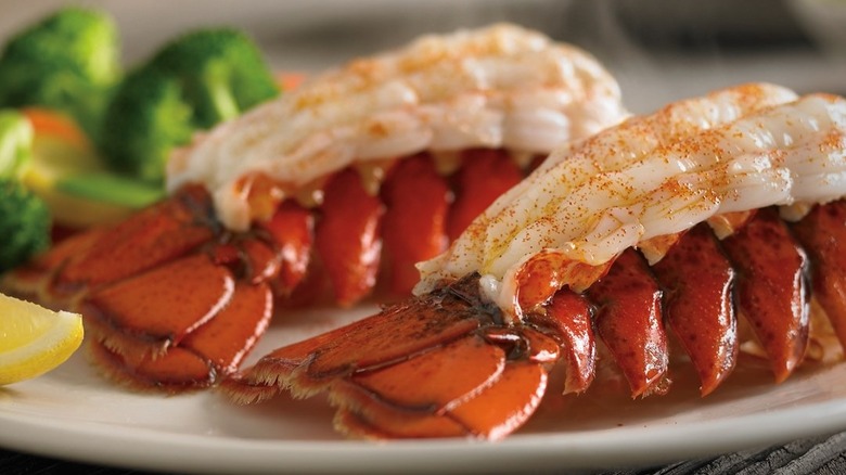 Two lobster tails from Outback Steakhouse next to wedge of lemon and vegetables