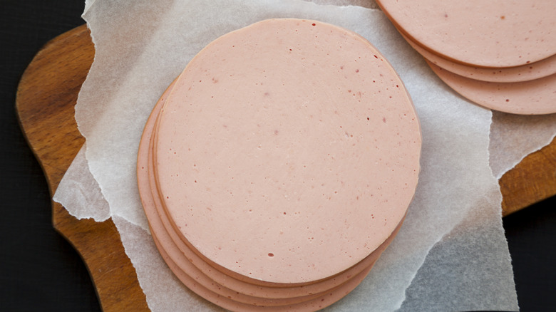 Sliced bologna sitting on parchment paper on wooden cutting board and black background
