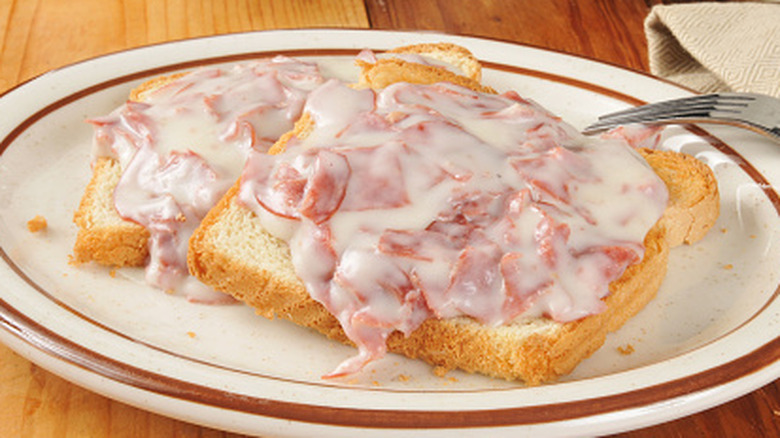 A close up of a diner dish of creamed beef on toast, plated on a wooden table
