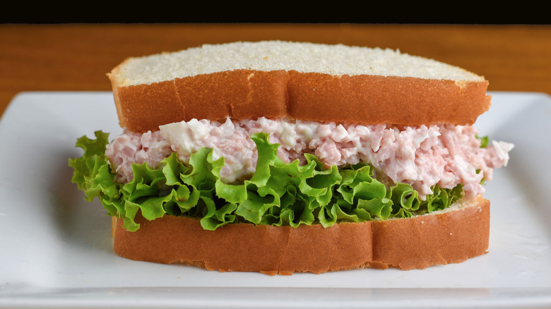 Close-up of a deviled ham salad sandwich with lettuce on white bread, white plate, and wooden table