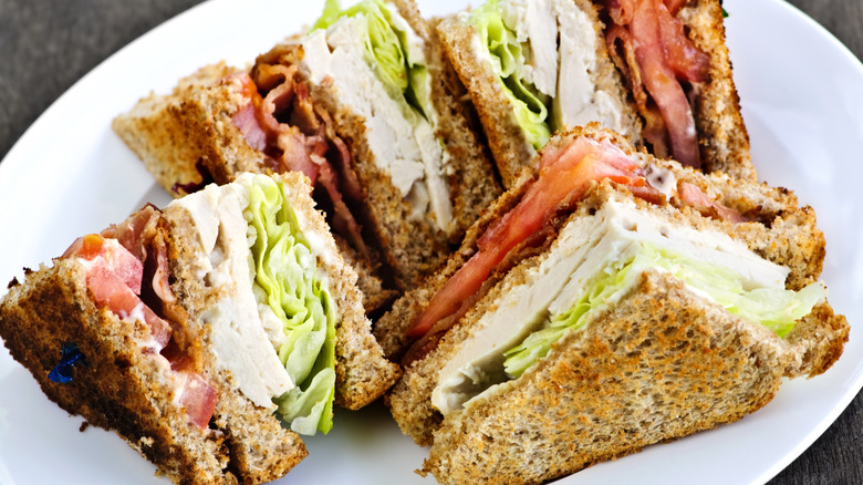 A close-up of a club sandwich on a white plate with a dark table