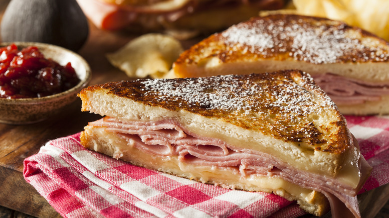 Close-up of a Monte Cristo sandwich and raspberry jam, sitting on a gingham napkin and wooden board