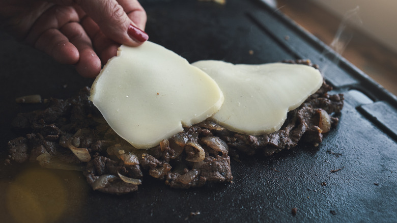 Close-up of steak and onions on the grill being topped with cheese to melt