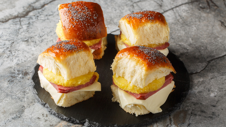 Four small ham and pineapple sandwiches on a black plate and marbled background