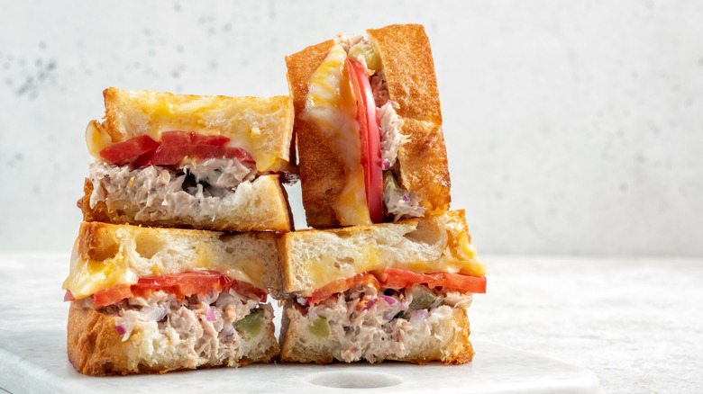 Close-up of a tuna melt with tomato on white bread, sitting on a white counter and background