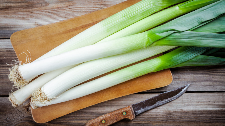 leeks on a wooden cutting board next to knife