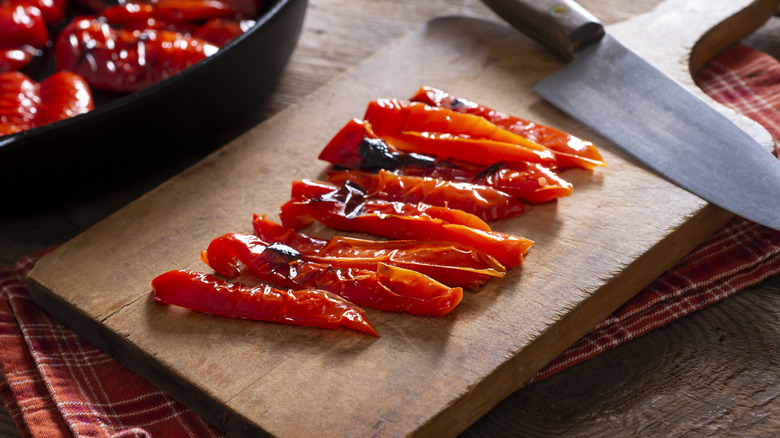 Sliced roasted red peppers on wooden cutting board with knife