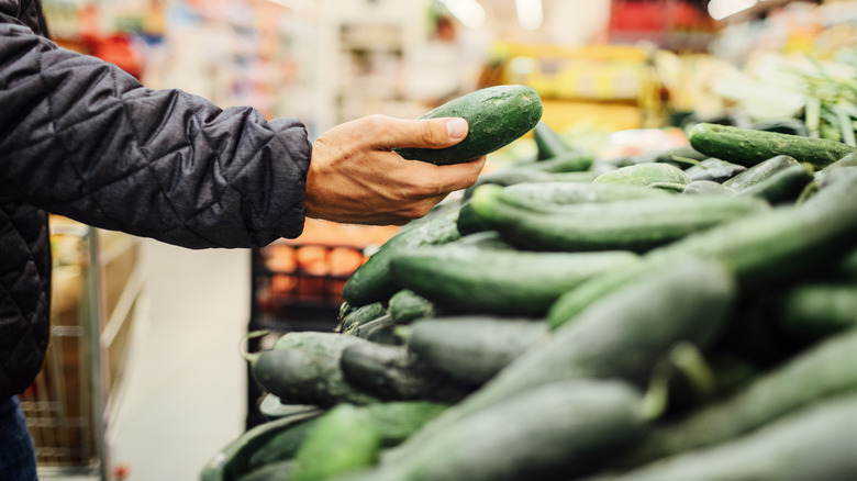 person choosing cucumber at grocery store