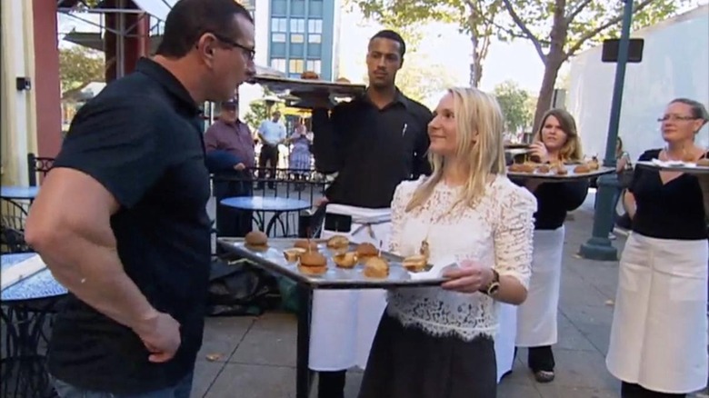 Robert Irvine speaks to a server holding a tray of food outside restaurant