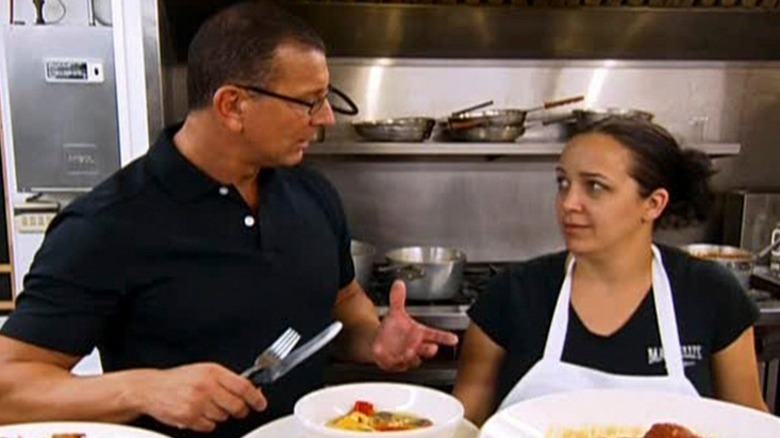 Robert Irvine speaking to chef in front of food in Mainelli's kitchen