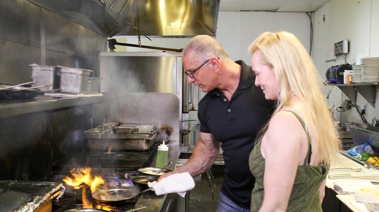 Robert Irvine teaching staff member how to cook in restaurant kitchen