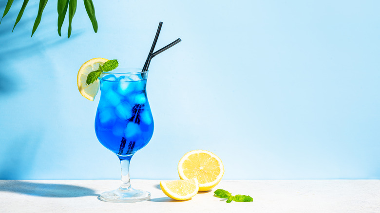 blue lagoon cocktail against blue background with chopped lemon and mint leaf