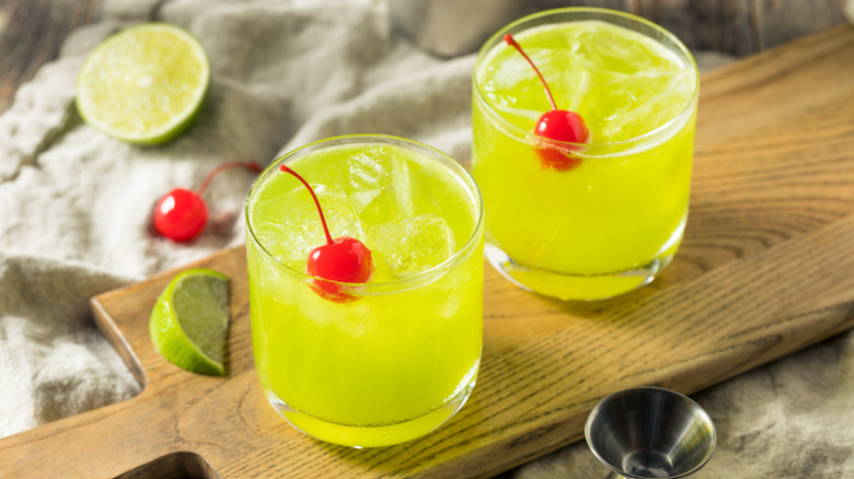 two glasses of midori sour with cherries on wooden board