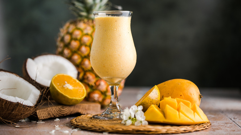Pina colada pineapple cocktail on rustic table with coconuts and pineapples in background
