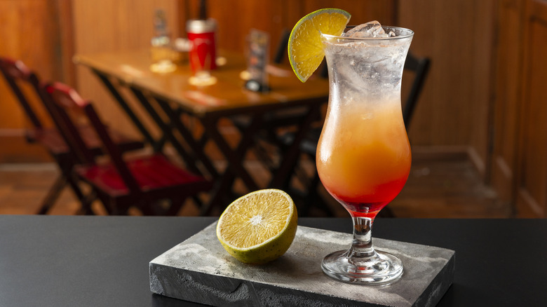 Sex on the beach cocktail with lime wedge on a bar next to half cut lime with table in background