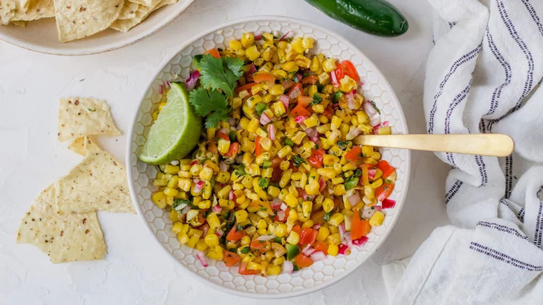 Roasted Corn Salsa in white bowl with lime and spoon