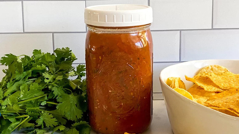 Jar of spicy salsa roja next to cilantro and chips