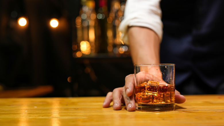 A bartender placing a glass of whiskey down on to a table