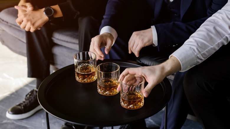 Three people sitting next to each other with three glasses of whiskey set out on a table in front of them