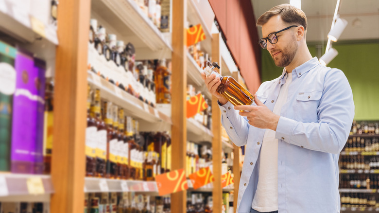 A person in a liquor store, checking out the label of a bottle of whiskey