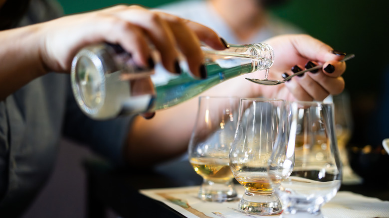 A person carefully pouring water on to a spoon to add it to whiskey