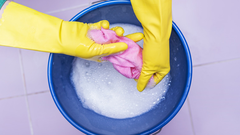 Wringing out cloth in bucket of soapy water